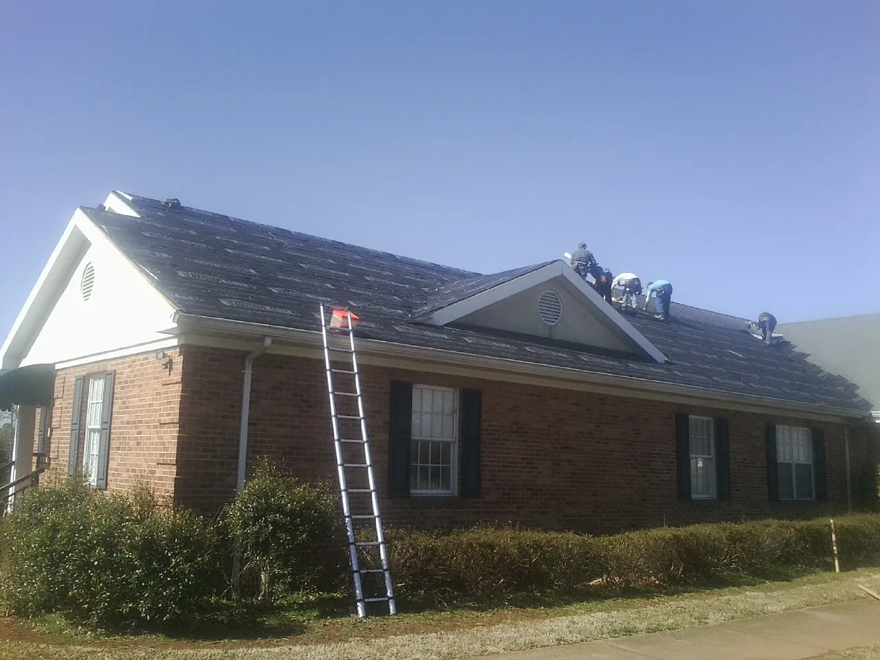 Crew tearing shingles off a brick ranch roof with a ladder set — Emergency Roof Repair work by our crew in Graceville