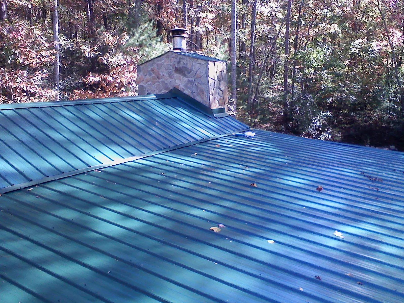 New green metal roof and stone chimney surrounded by autumn woods in Graceville