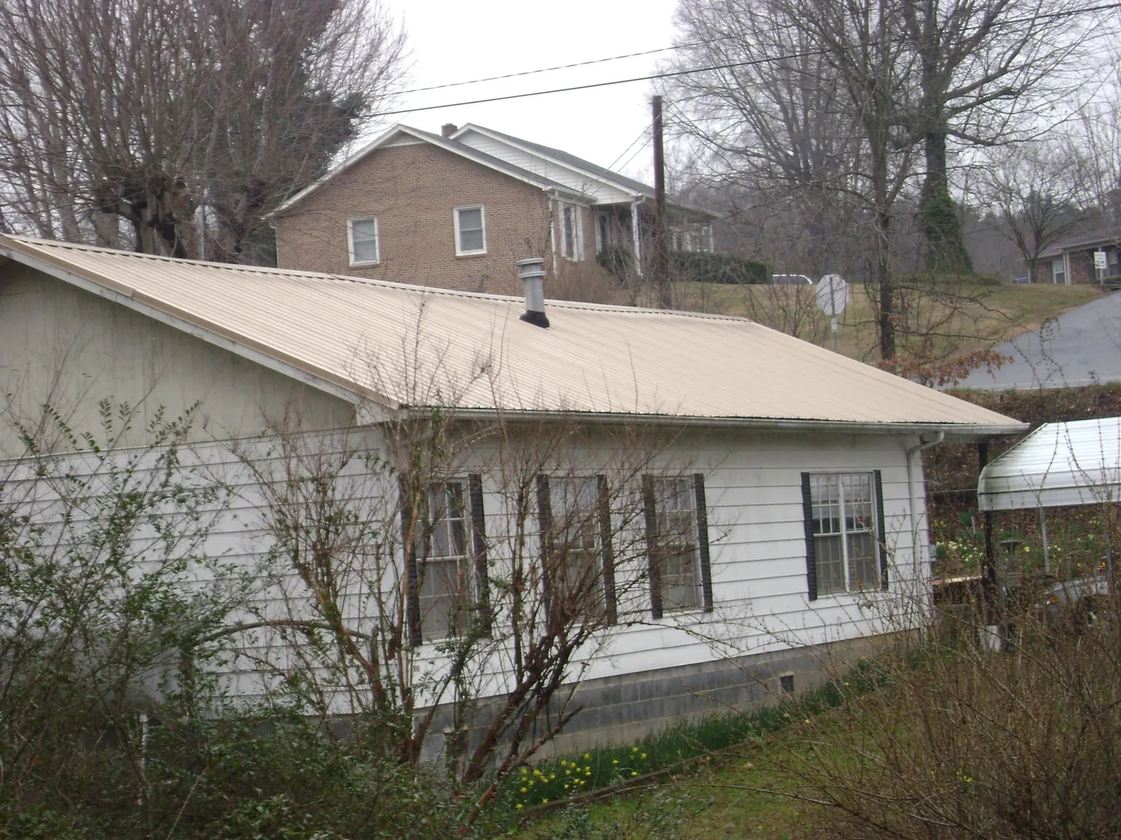 Tan metal roof on a white sided house set into a hillside — Commercial Roofing by Roofing Brothers in Graceville