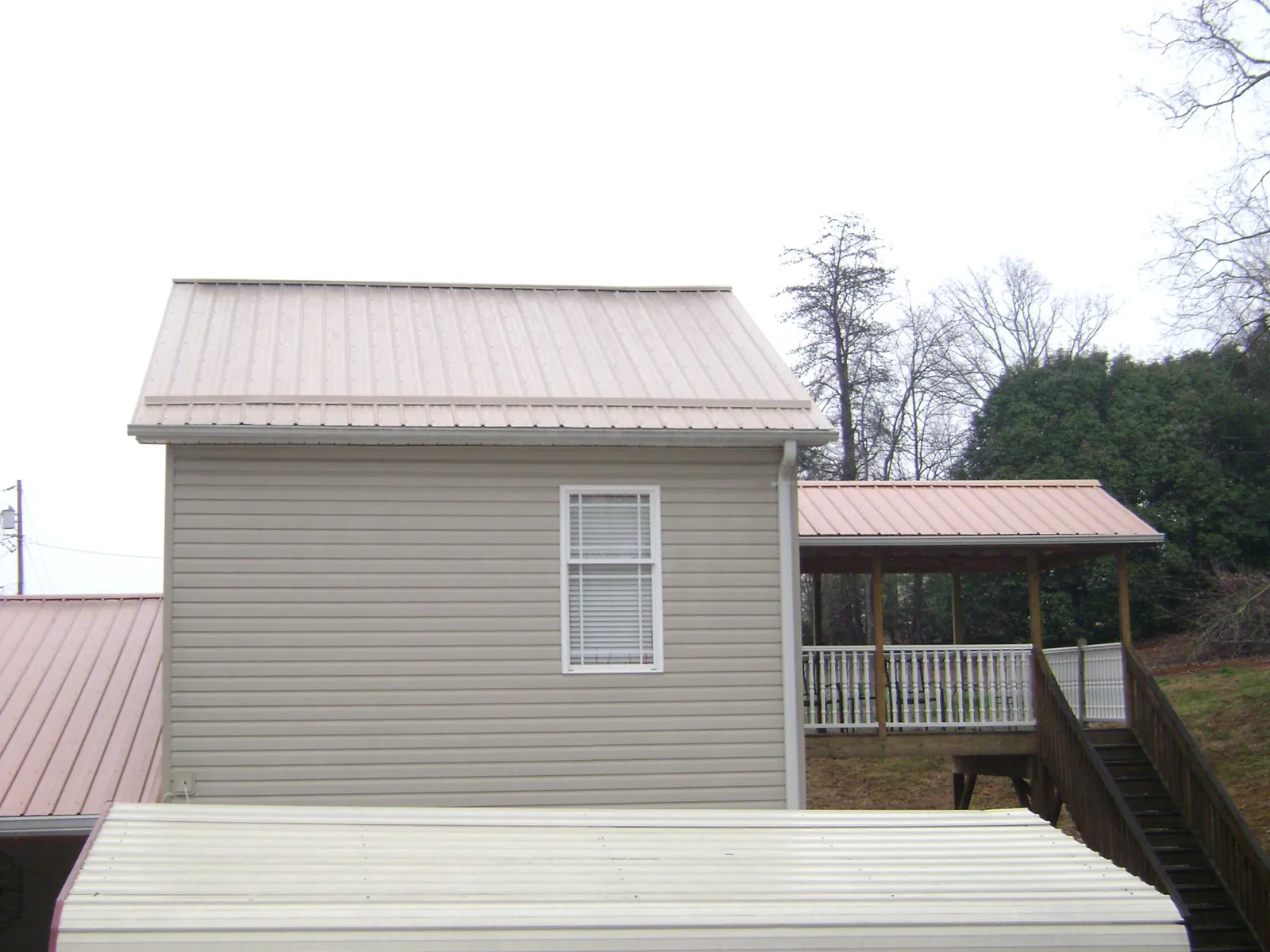 Tan metal roofs on a two story addition and attached porch, from a Roof Replacement job in Graceville